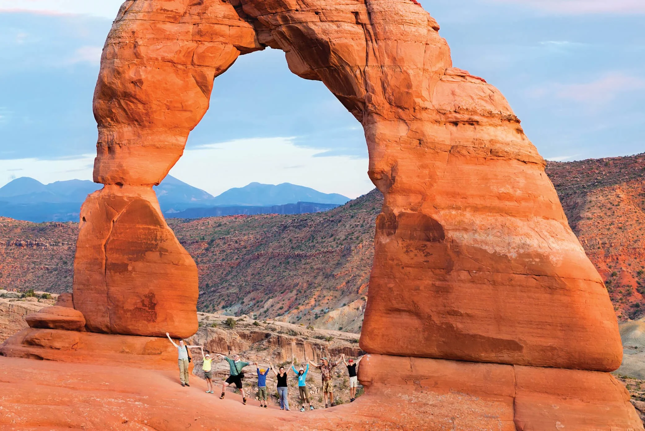 A family celebrating under a massive natural stone arch in the American West; a signature multi-generational discovery curated by Willow & Wander Travel.