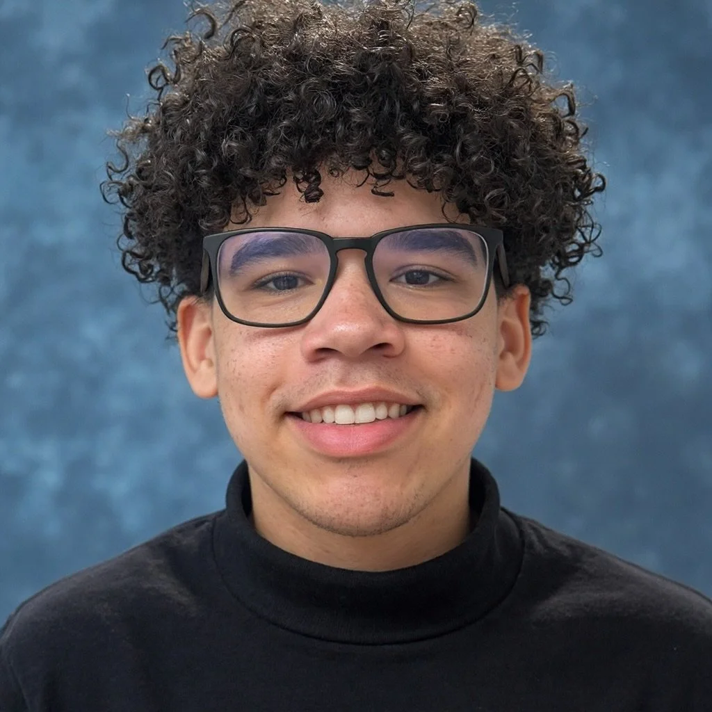 A smiling young man with curly hair, glasses, and a black turtleneck shirt against a blue textured background.