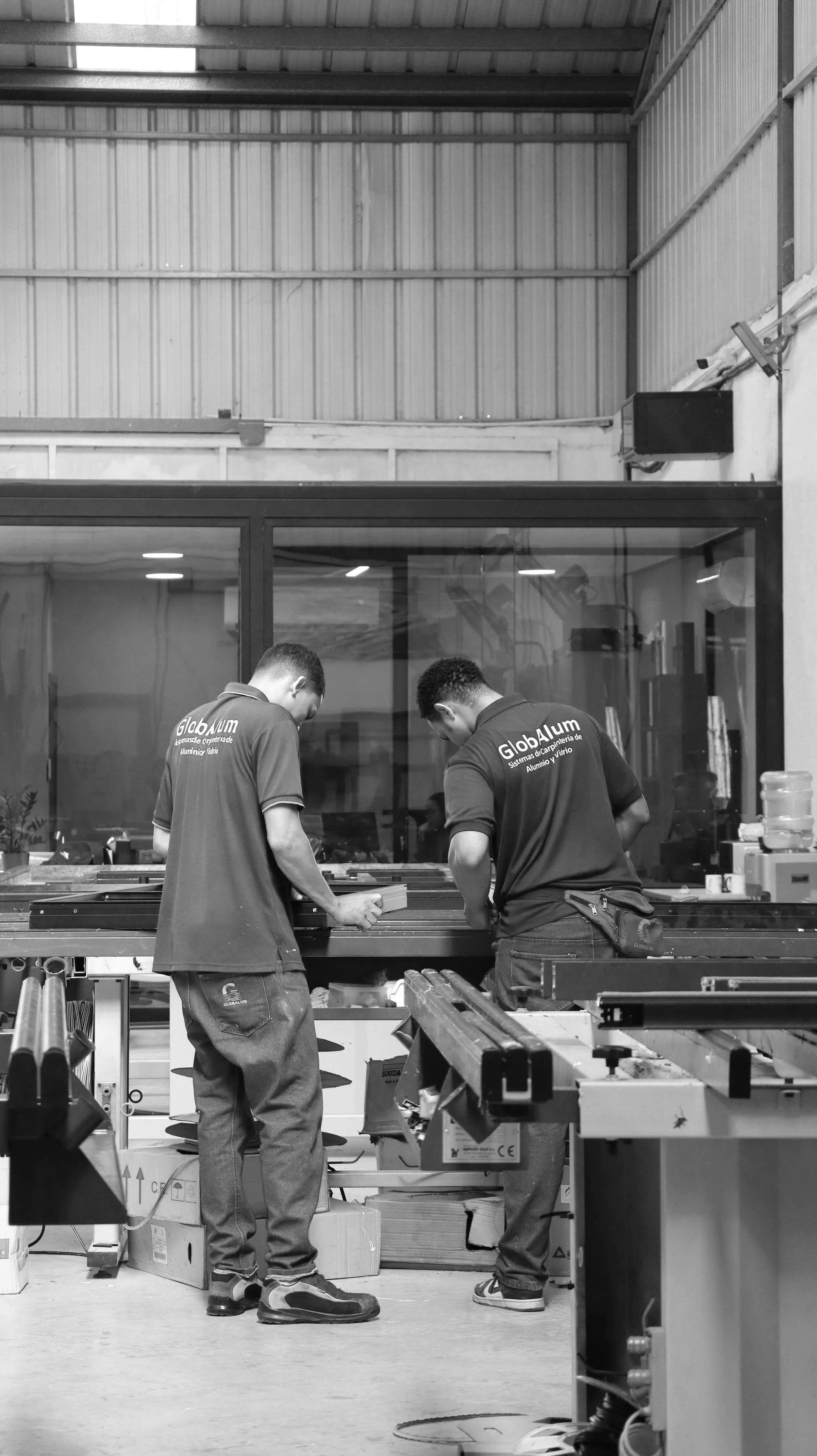 Two workers wearing branded shirts working on electrical or lighting components in an industrial or warehouse setting.