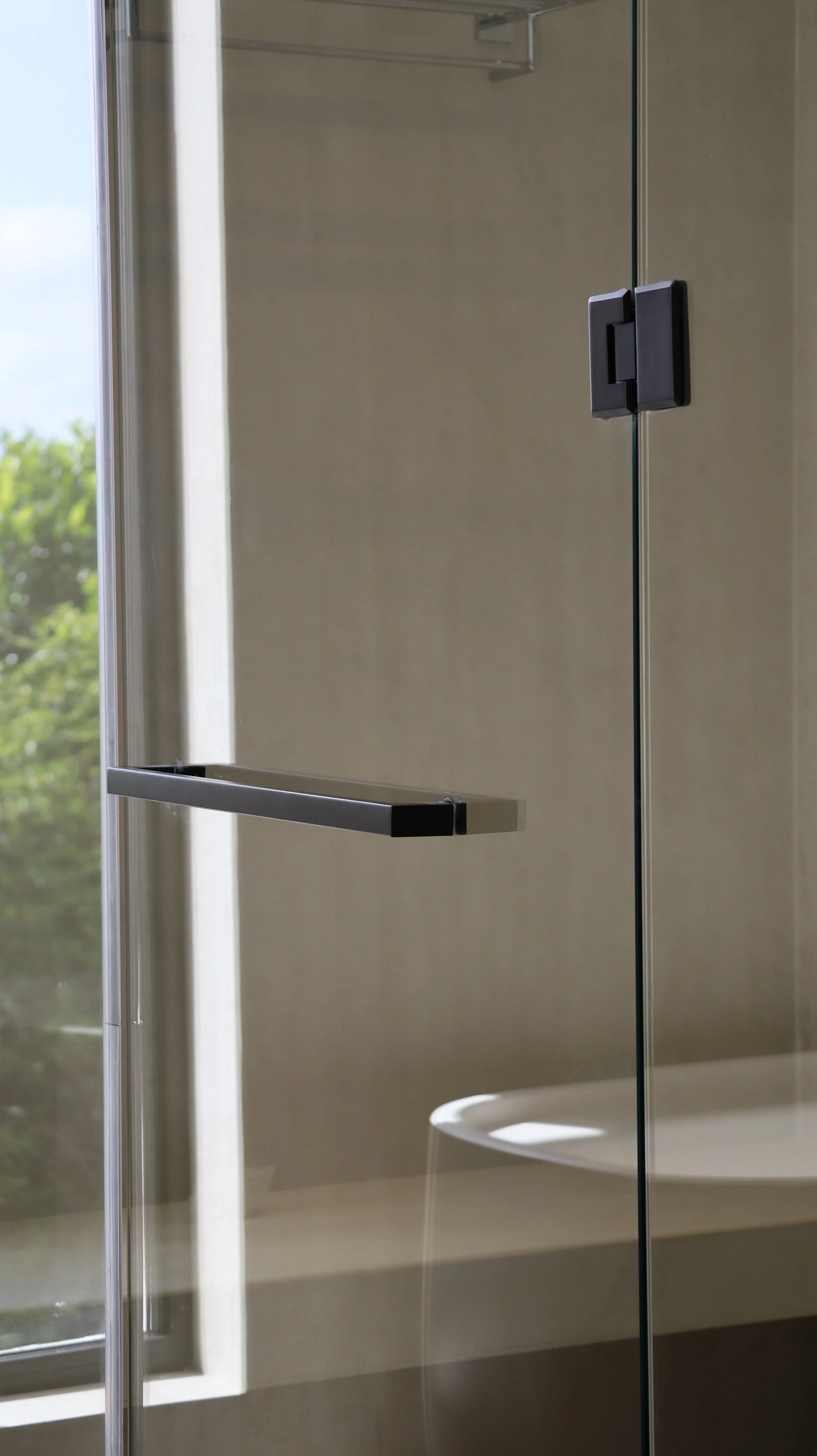 Interior view of a modern shower with glass walls, a metal grab bar, a black handle, and a view of a white toilet inside the bathroom.