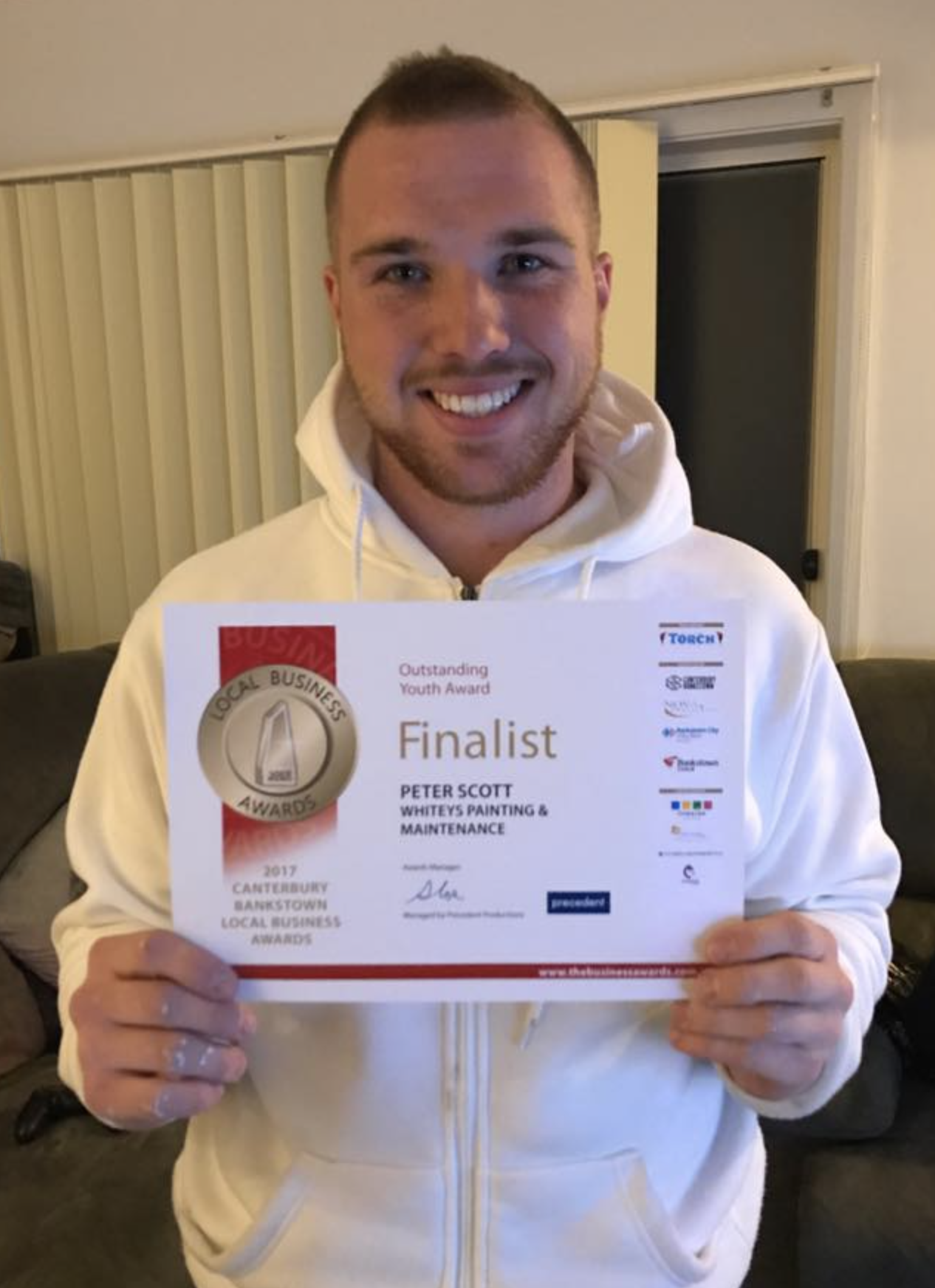 A smiling man holding a certificate for being a finalist in the 2017 Canterbury Bankstown Local Business Awards, for his painting and maintenance business.