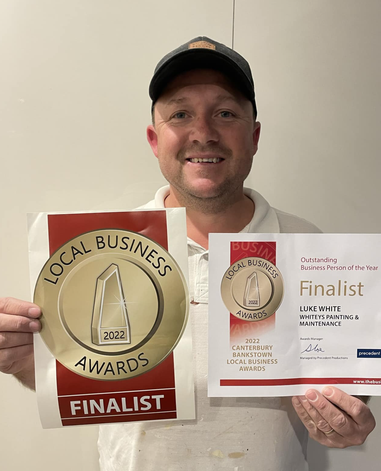 Man smiling holding an award poster and a certificate for being a finalist in the 2022 Local Business Awards.