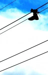 A pair of boots framed by a blue sky hangs from electrical wires.