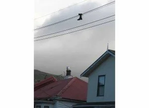 Black boot hangs from power line above rooftops of small town.