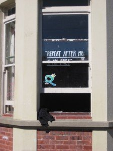 Partially opened corner window with lettering, “Repeat after me, I am free.” Partially opened corner window with lettering, “Repeat after me, I am free.”