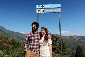 Nathan and Sarah embrace under a road sign labeled “Wedding Ring” with an arrow that seems to be down at them.