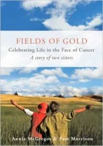 Book cover of “Fields of Gold: A story of two sisters,” by Pam Morrison. The cover is a photograph of two women with open arms, backs towards us, looking out on a golden field and blue sky.