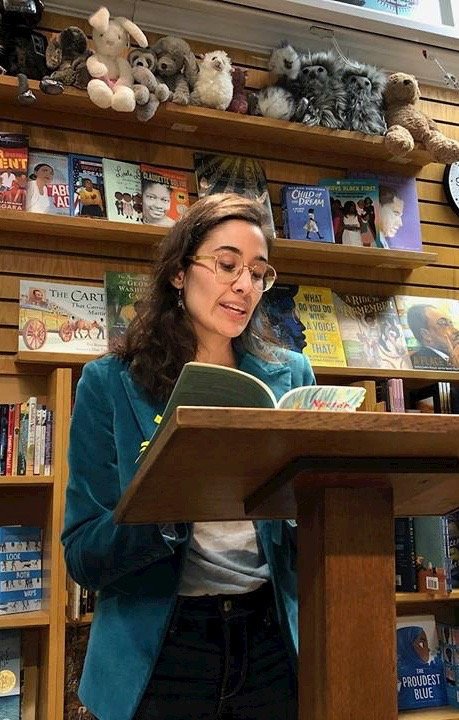 Jacqueline Balderrama doing a book reading at a podium in the children’s section of a bookstore.