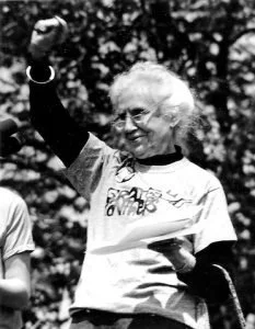 Maggie Kuhn, the gray panther, wearing an old tee-shirt raises her fist in solidarity.