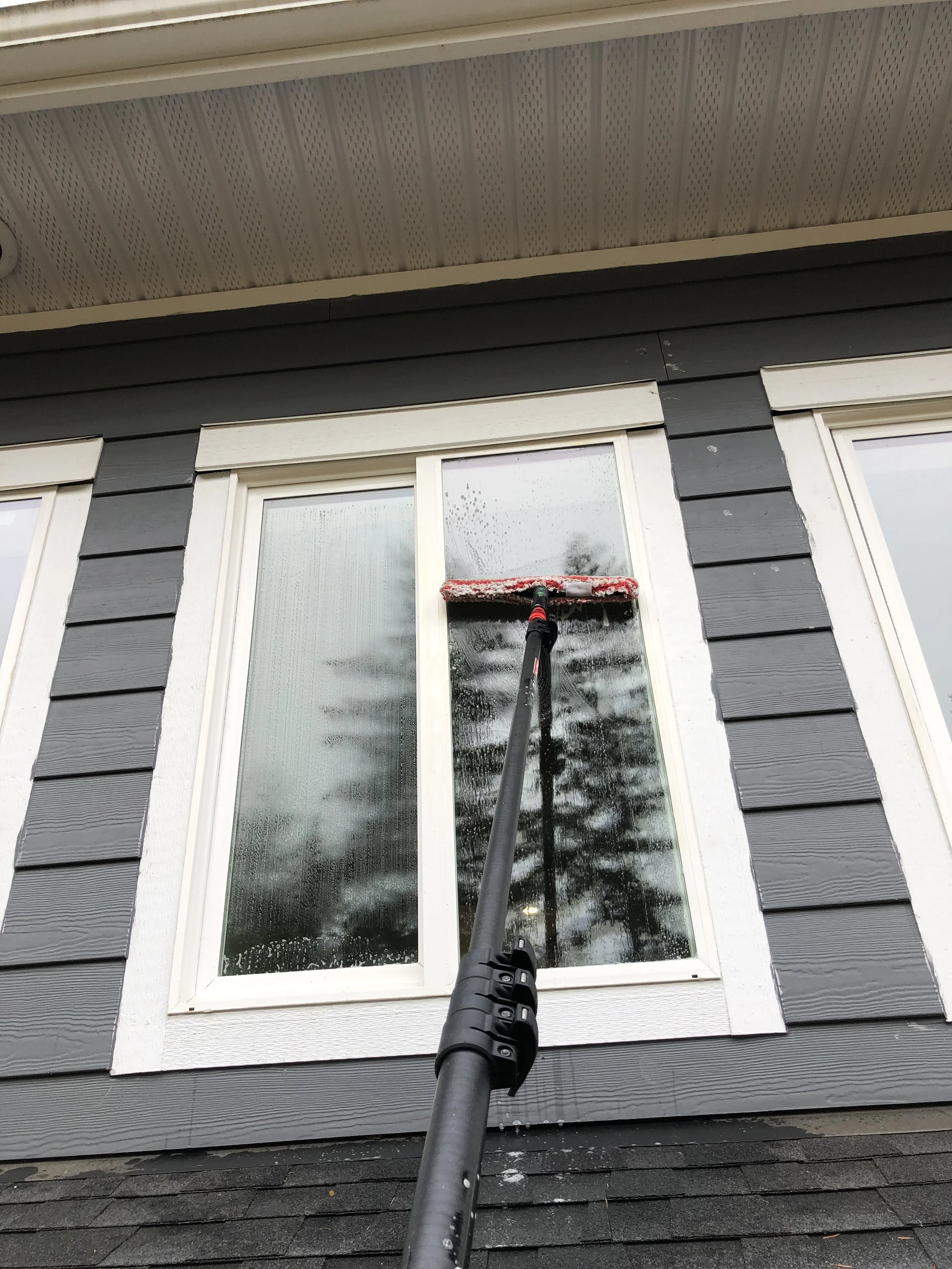 A window being cleaned on the exterior of a house with black and white siding.
