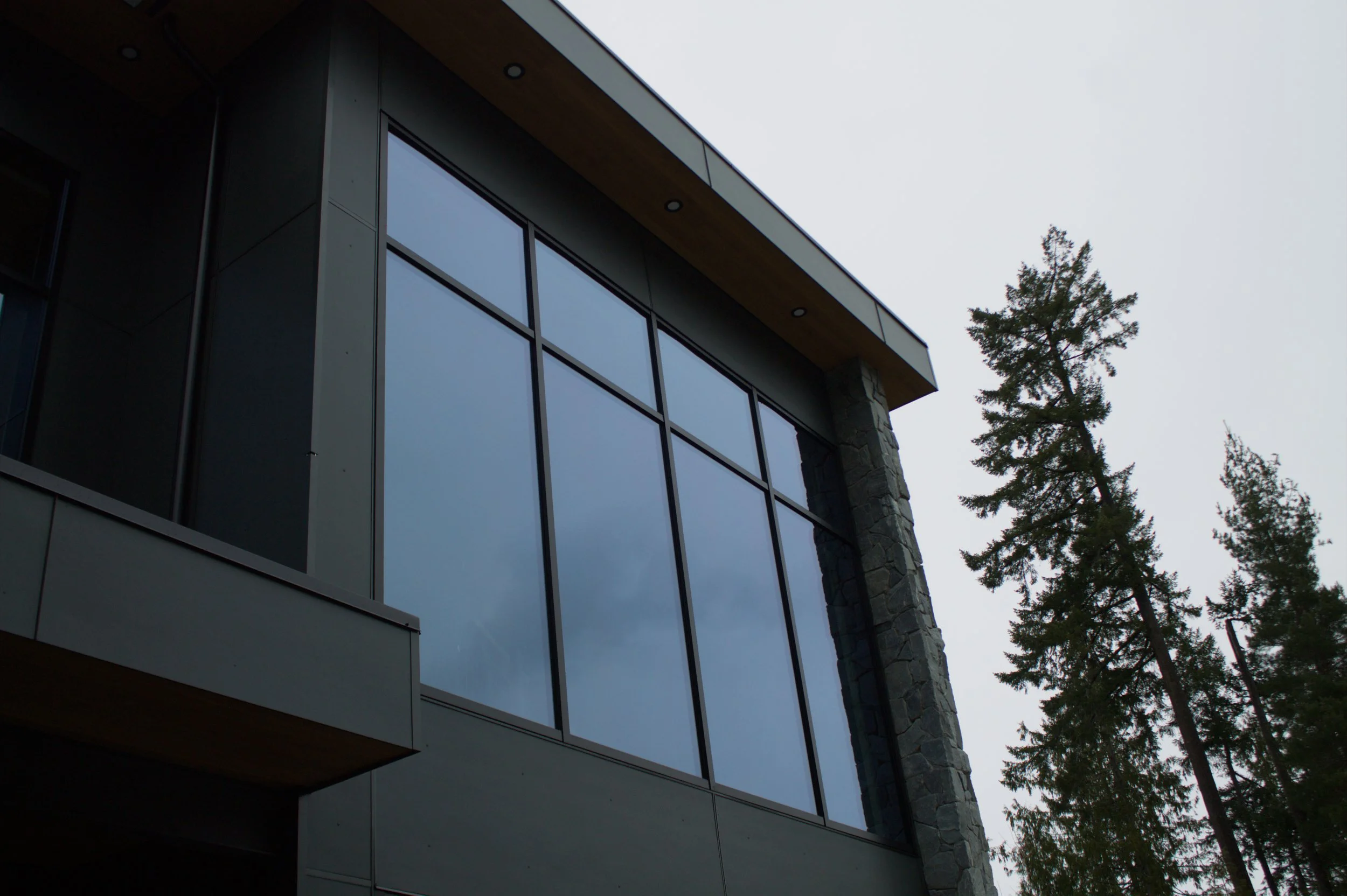 Modern building with large glass windows, stone pillar, and trees in the background, cloudy sky.