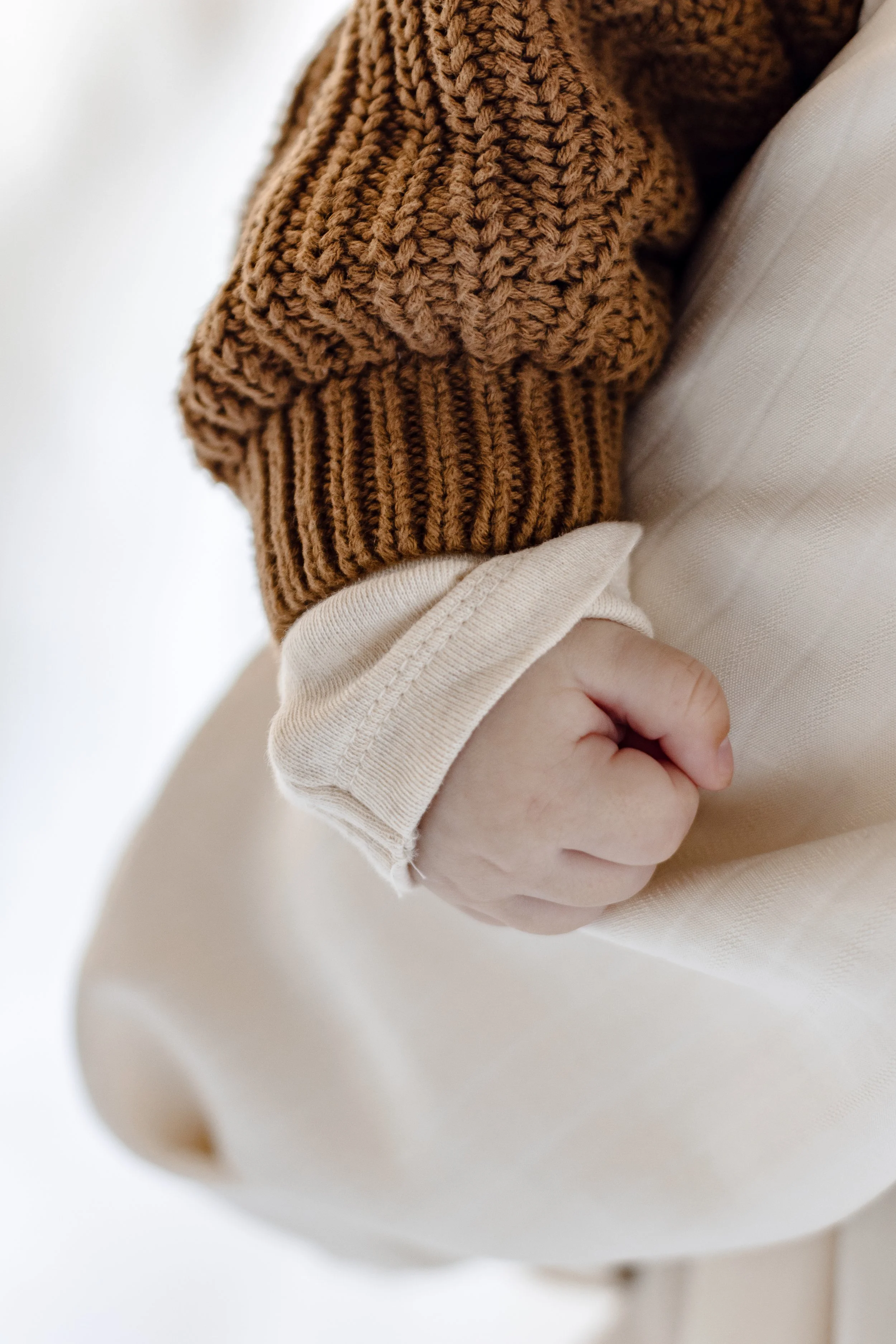 Close-up of a person's hand clenched into a fist, wearing a beige long-sleeve shirt and a brown knit sweater sleeve.