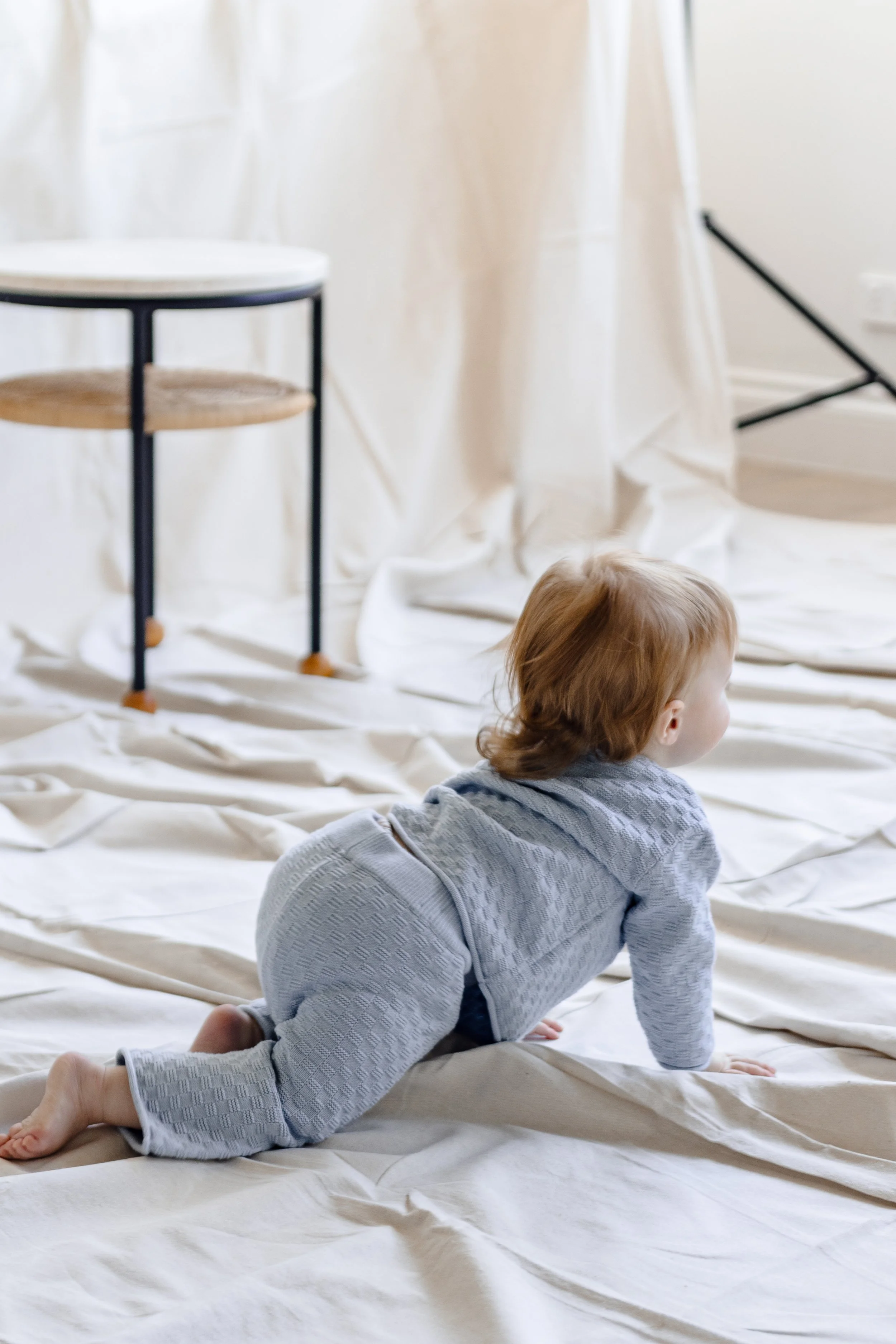 A young child with red hair crawling on a cream-colored fabric-covered floor in a bright room.