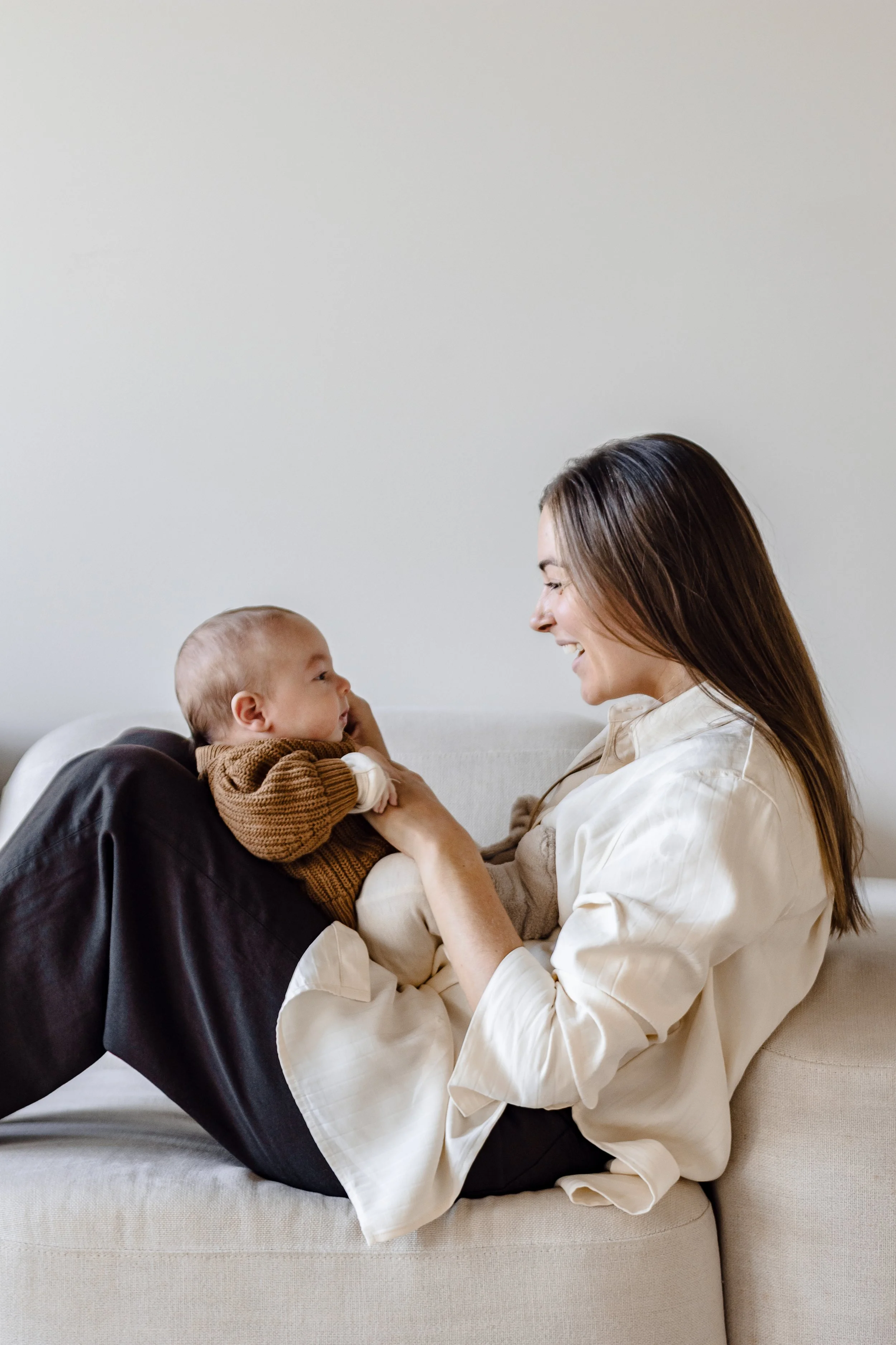 A woman lying on a sofa, holding and smiling at a young child.