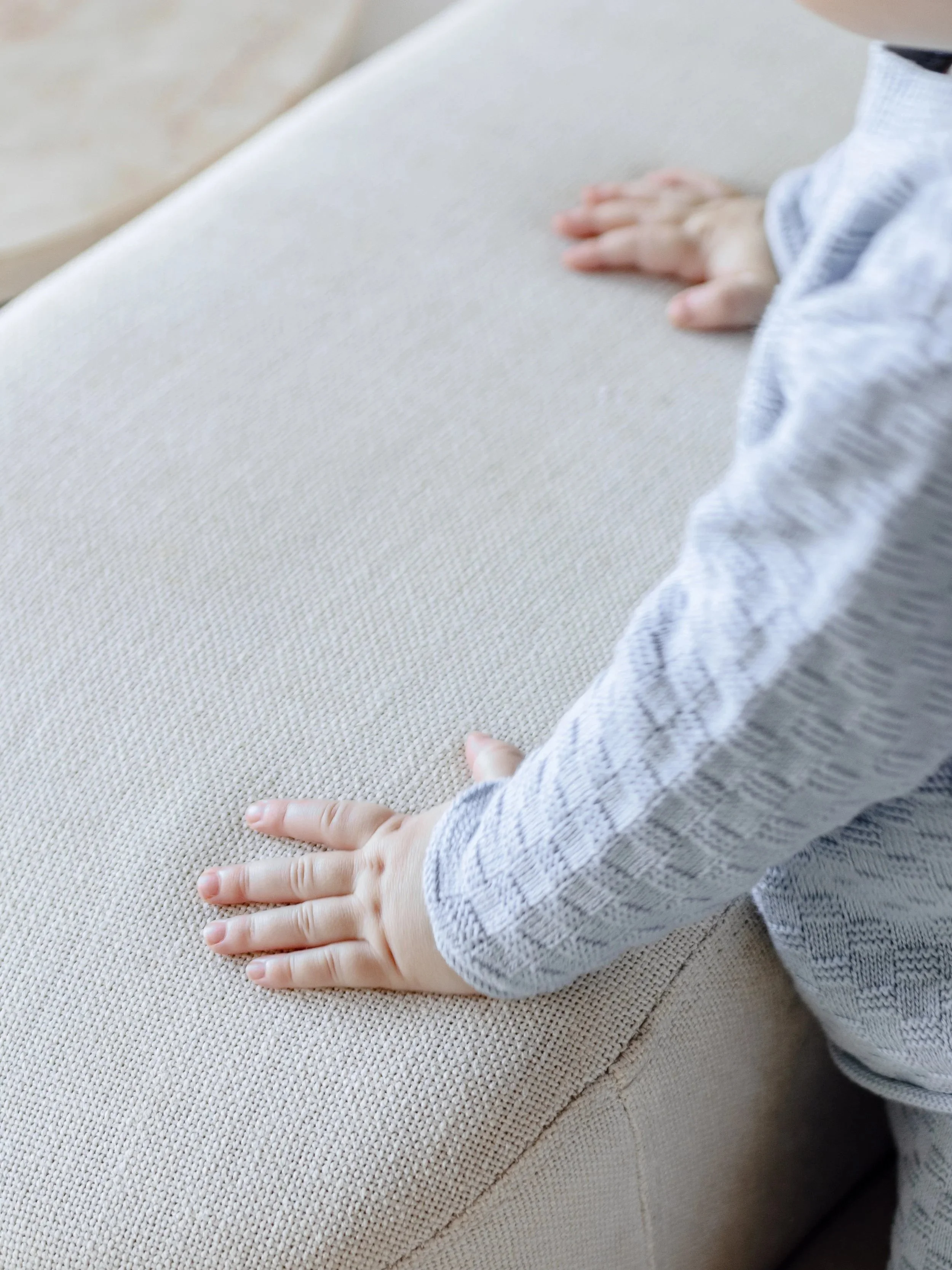 Close-up of a child's hands pressing on a beige fabric surface, likely a couch or cushion.