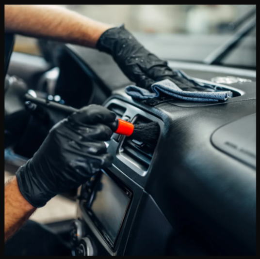 Person in black gloves cleaning car vent with a small brush.