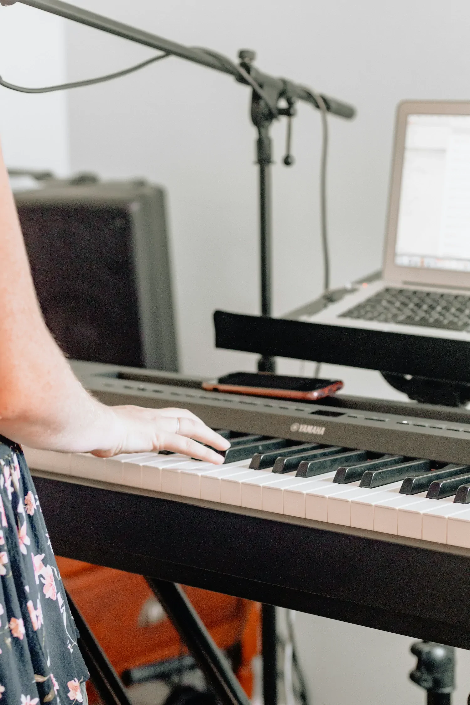 Someone playing an electronic keyboard in front of an open laptop.
