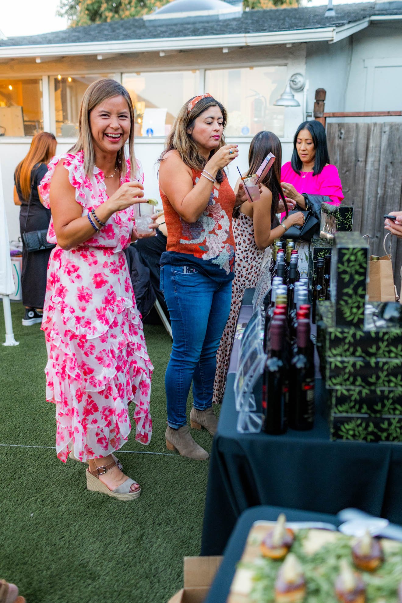 A group of women at an outdoor gathering browsing bottles of wine and enjoying drinks.