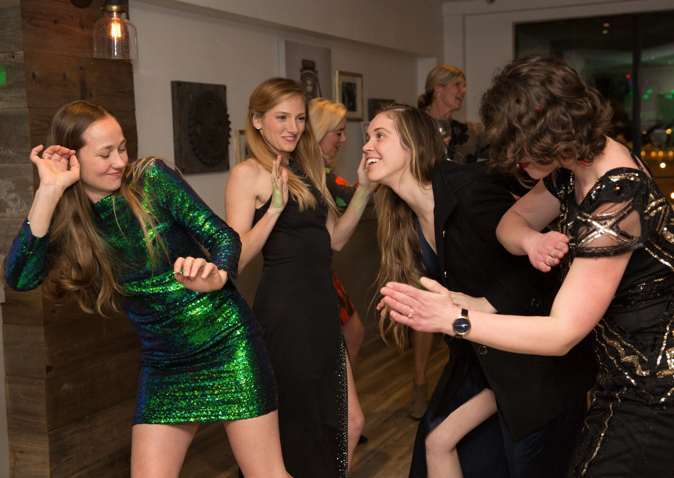 Group of women dancing and laughing at an indoor party or celebration.