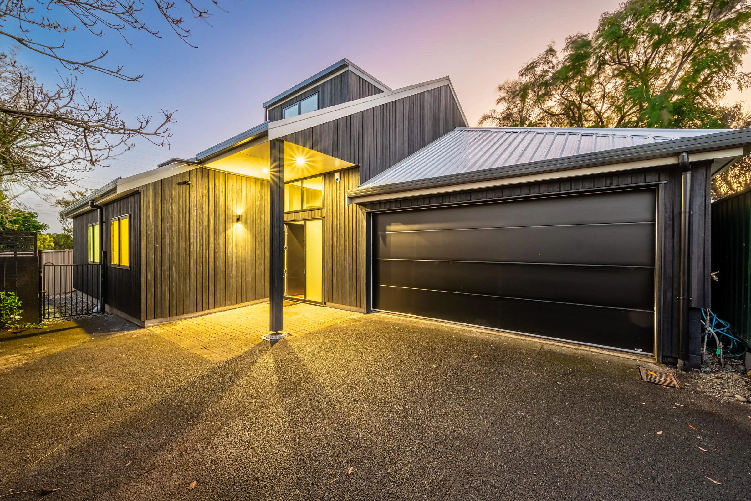Modern black house with a garage and a small front yard during twilight.