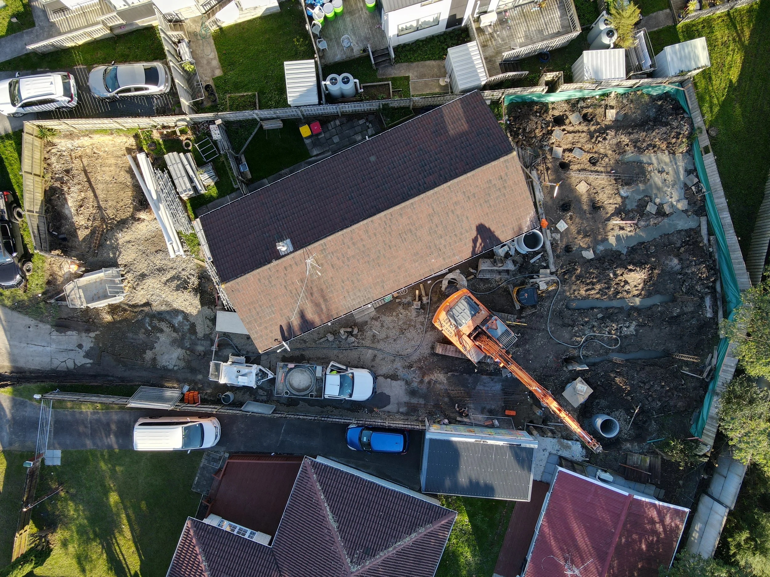 An aerial view of a construction site next to a house, with excavation equipment and construction materials, in a residential neighborhood.