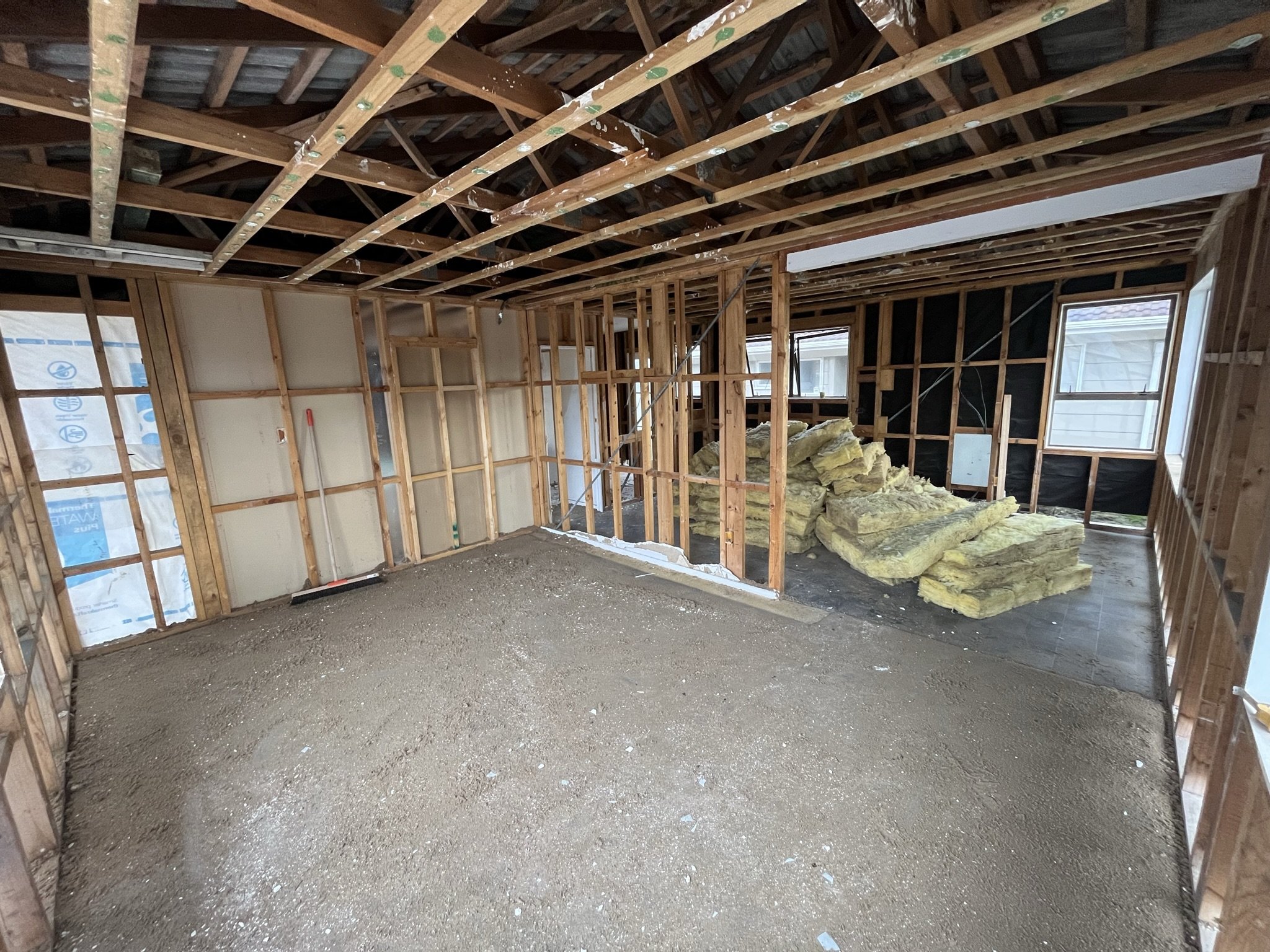Interior of a house under construction with exposed wooden framing, insulation materials on the floor, and holes for future windows.