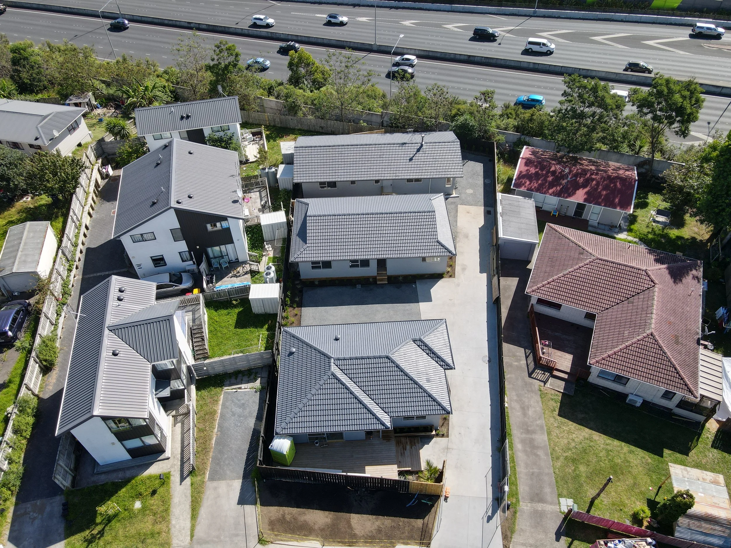 Aerial view of a residential neighborhood with several houses, driveways, and yards, situated near a highway.