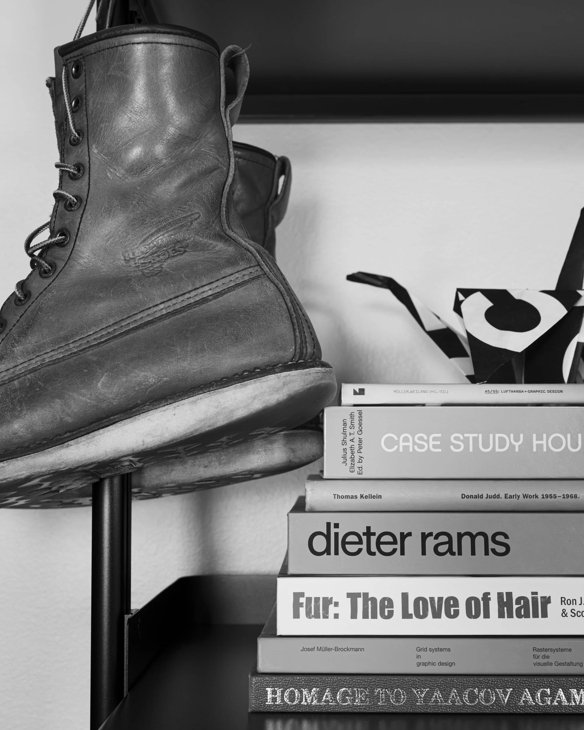 Stack of books on a shelf next to a black and white leather boot with laces, with a book titled "Fur: The Love of Hair" partially visible at the bottom of the stack.