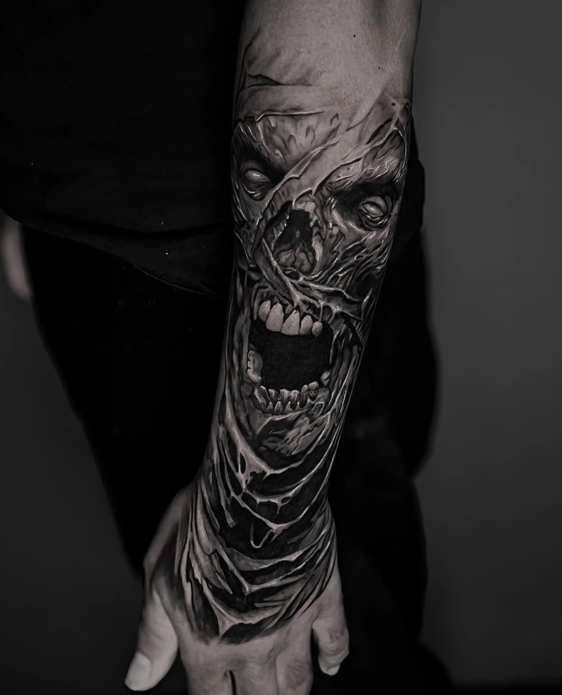 A person's arm with a detailed black and grey tattoo of an Egyptian mummy, extending from the wrist to the upper arm.