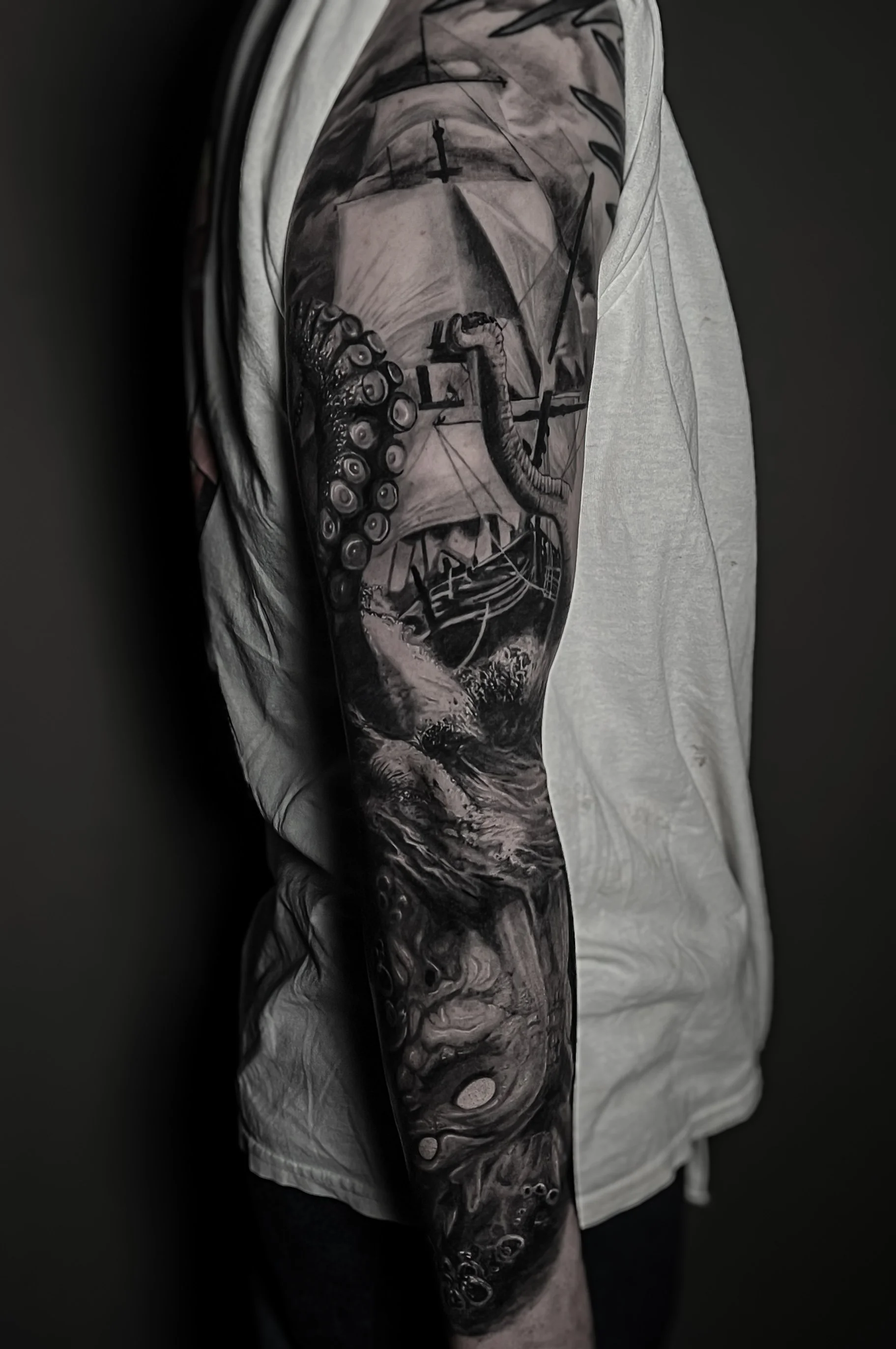 A person with a detailed black and gray tattoo sleeve on their arm, featuring a nautical theme with a ship's wheel, ropes, and ocean waves.