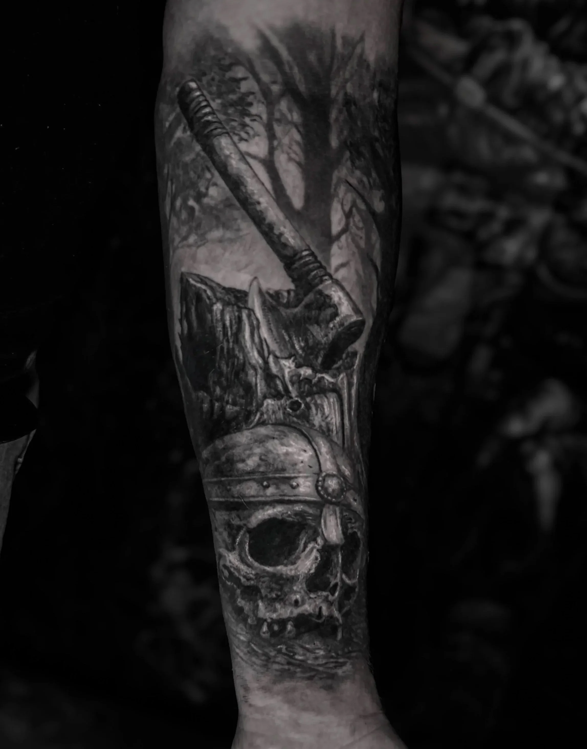 Black and white tattoo of a forest scene with an axe, tree stump and viking skull.