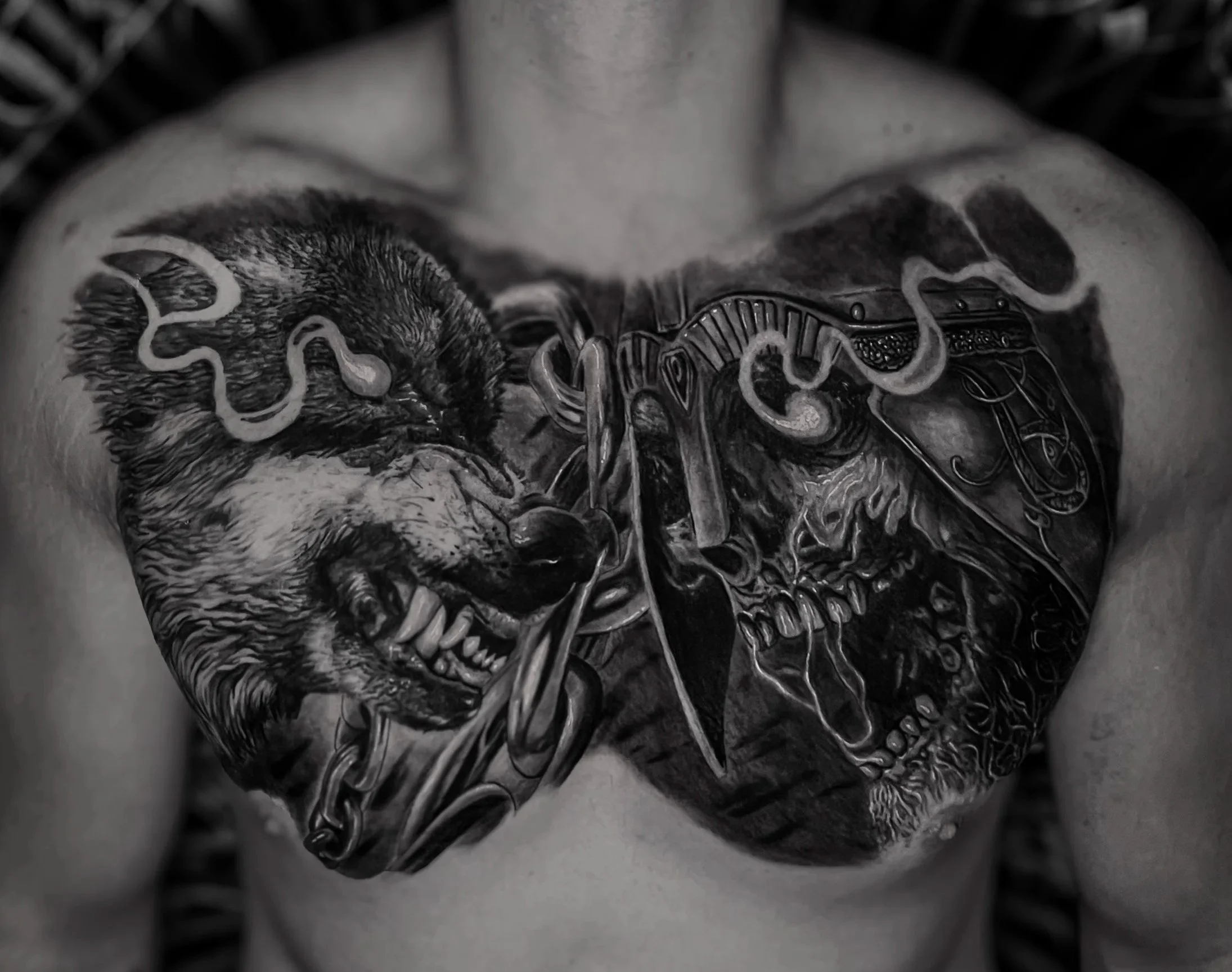 A black and white tattoo of a wolf's head and an undead viking on a person's chest, with intricate line work and shading.