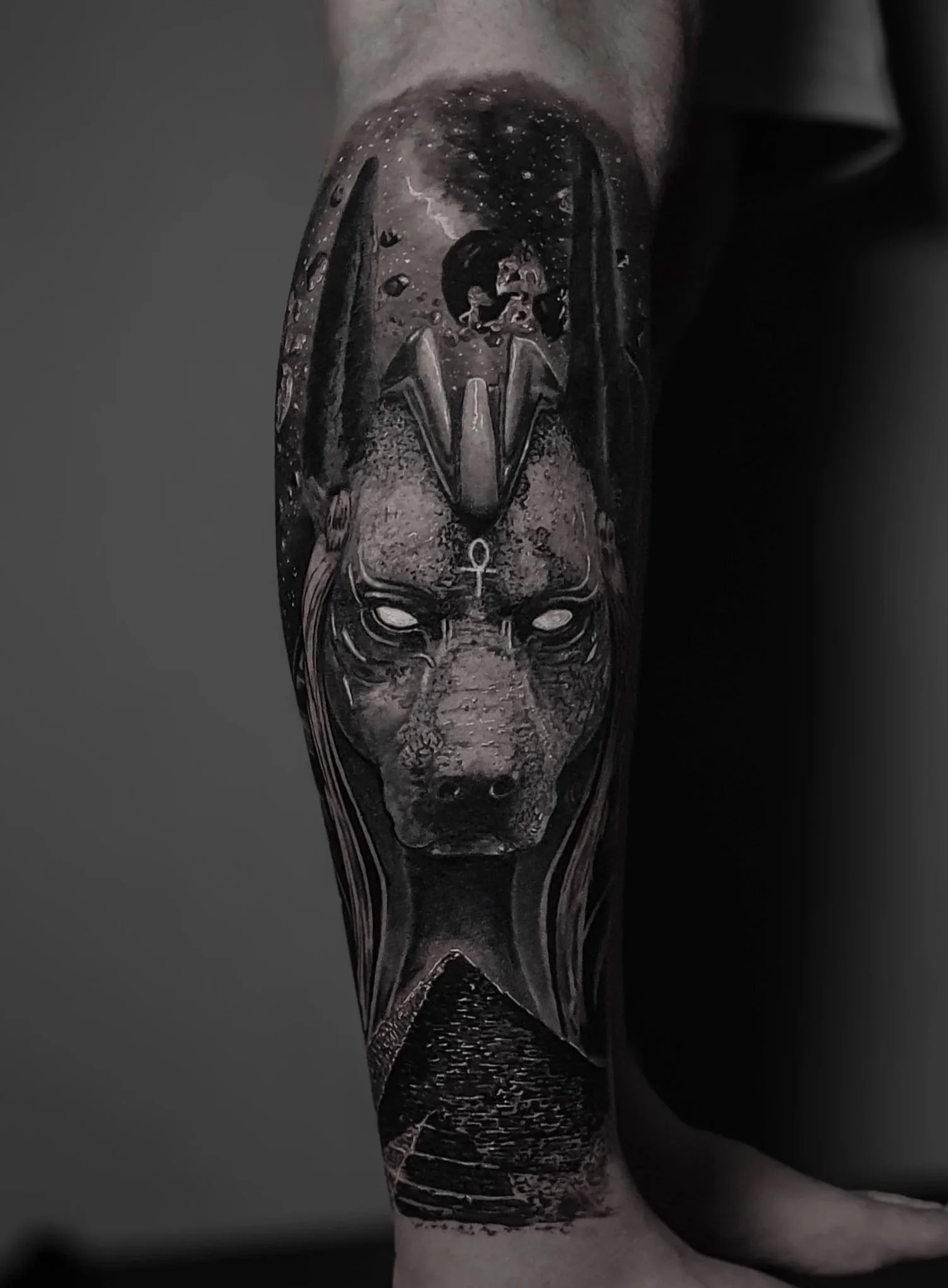 Tattoo of Anubis with celestial and space-themed elements, including stars and planets, on a person's leg.