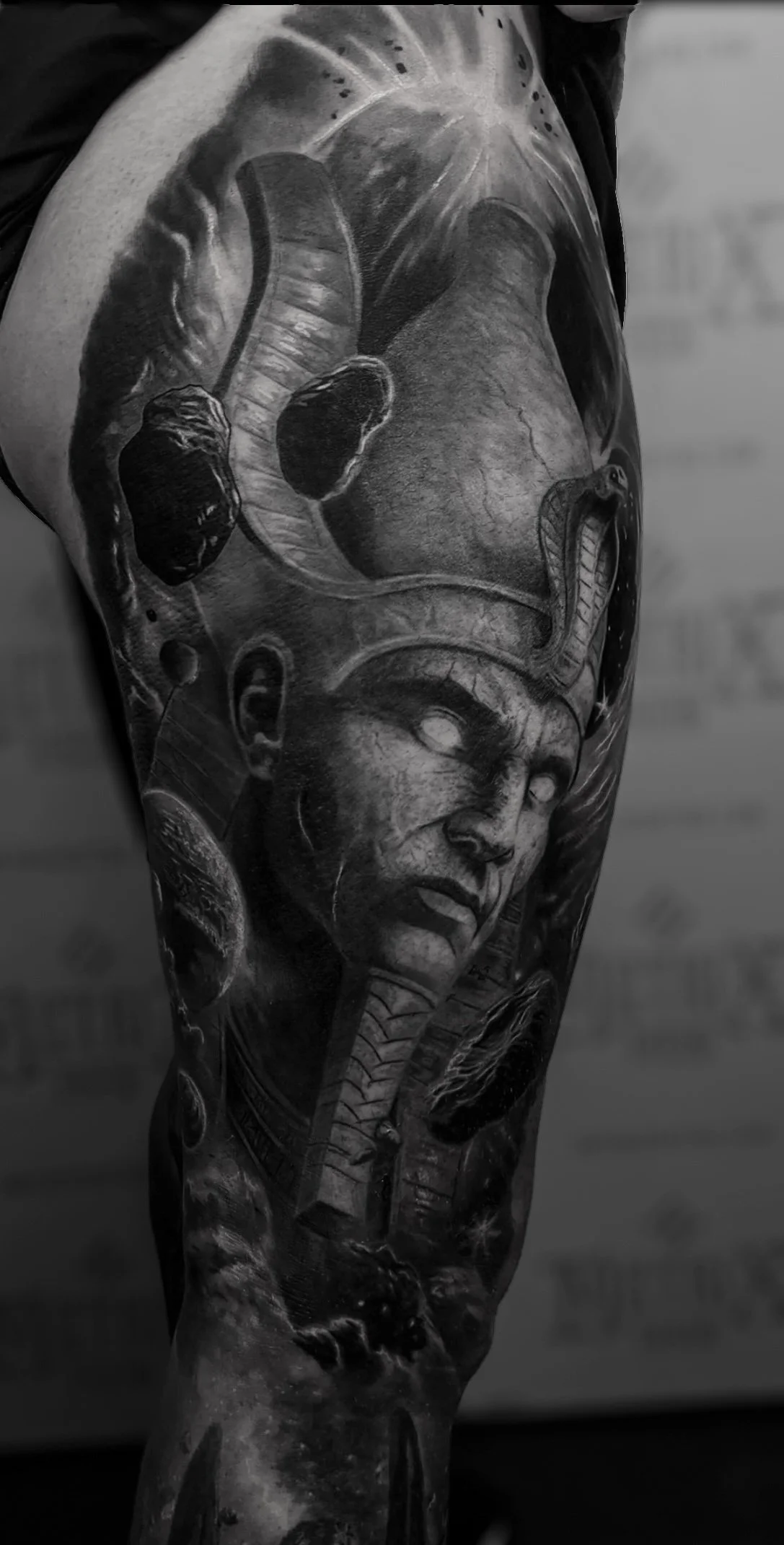 Black and gray tattoo of an Egyptian god with glowing eyes on a person's leg.