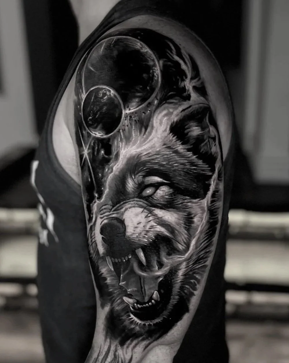 Black and grey tattoo of a snarling wolf's head on a person's arm, with detailed fur, fierce expression, planets and galaxy.