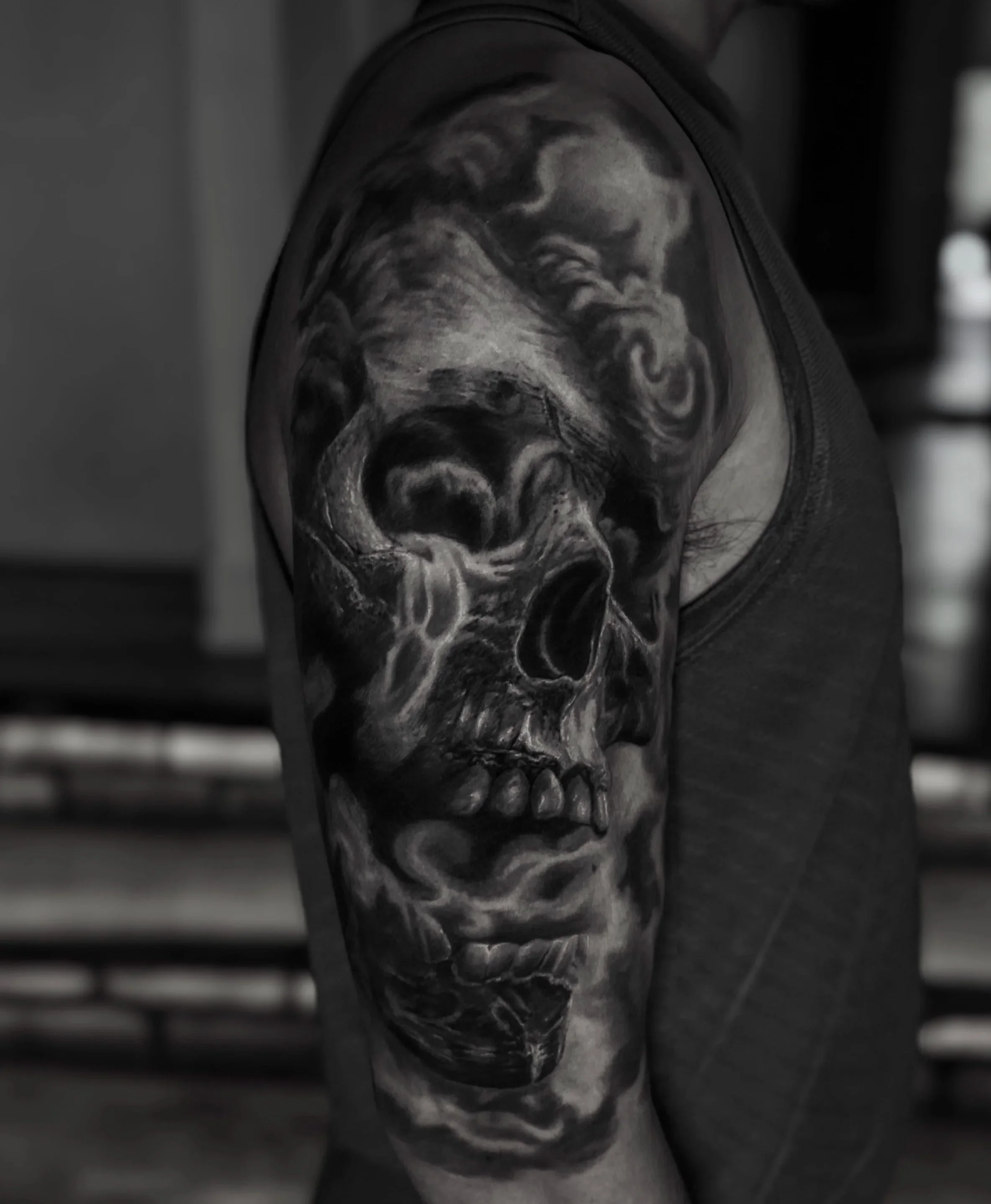 Close-up of a detailed black and gray tattoo of a skull and clouds on someone's arm.