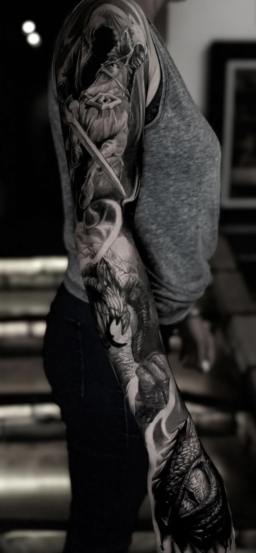 Close-up of a detailed black and grey tattoo sleeve on a person's arm featuring a Lord of the Rings wraith, balrog and dragon eye