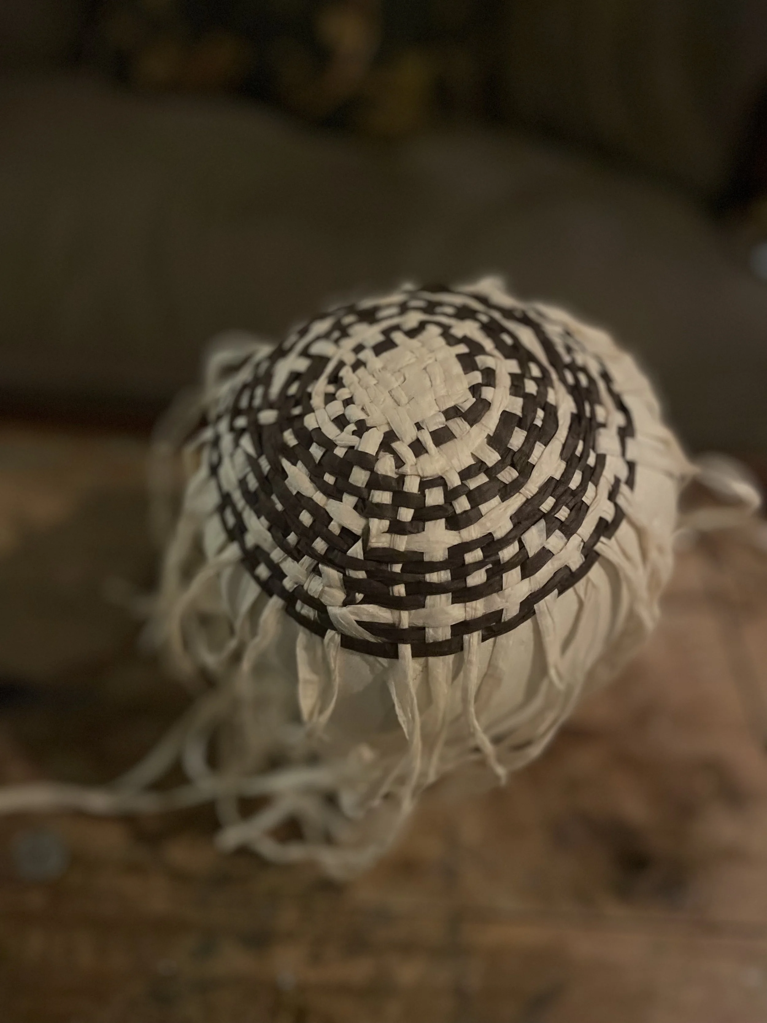 Close-up of a woven straw hat with a black and white spiral pattern on the top, placed on a wooden surface.