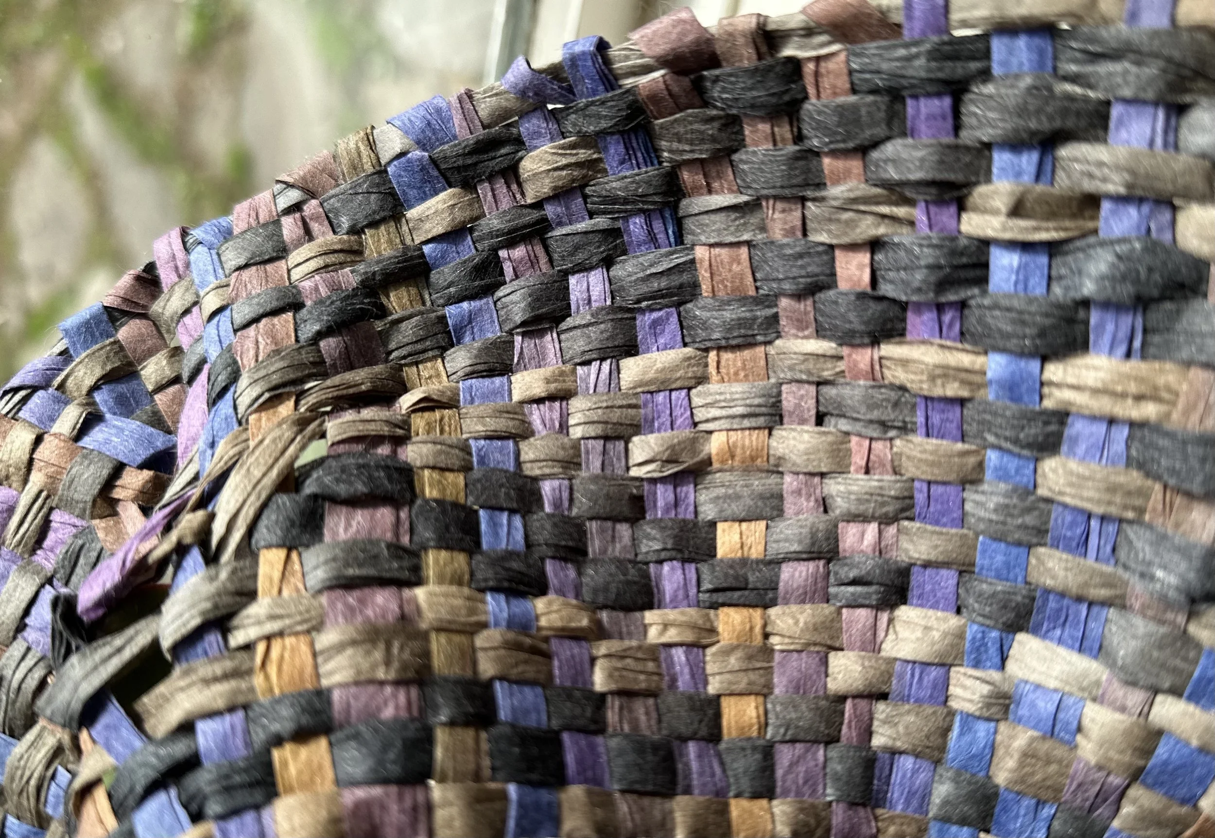 Close-up of a woven basket made of multicolored strips of material, including purple, blue, black, and brown.