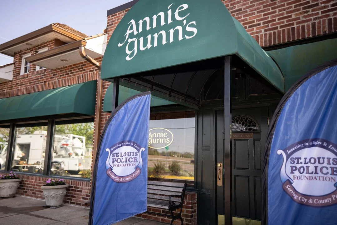 Exterior of Annie Gunn's restaurant with green awning, flags for St. Louis Police Foundation, and brick building.