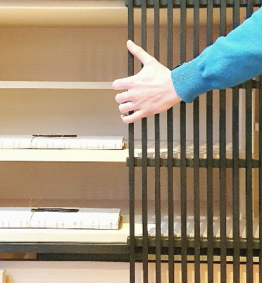 A person in a blue sweater is opening a black metal cabinet or cage with vertical bars.