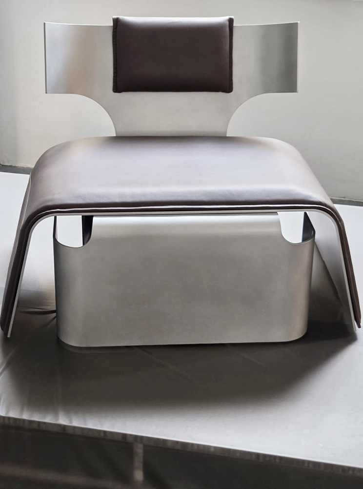 A modern chair with a metallic frame and a padded headrest, positioned against a neutral background.