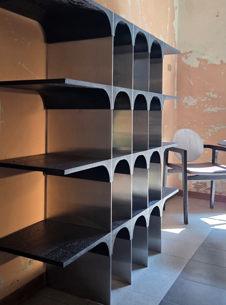 Empty black and metallic shelving unit in a room with a chair and peeling wall.