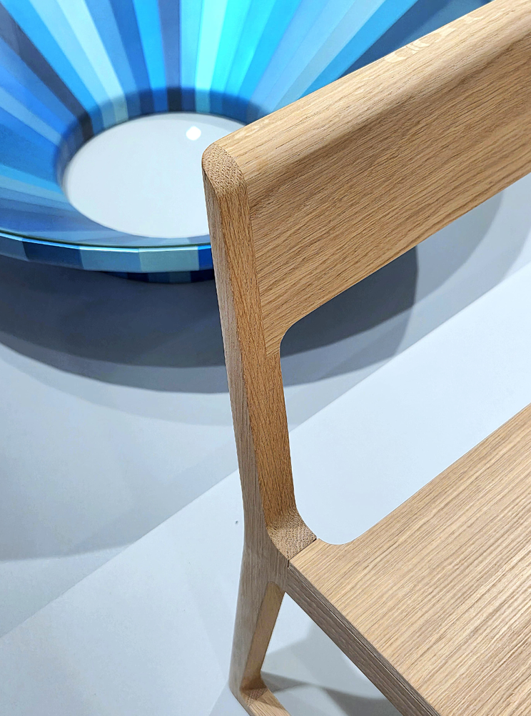 Close-up of a modern wooden chair with a curved backrest and seat, next to a blue bowl with a striped pattern inside.