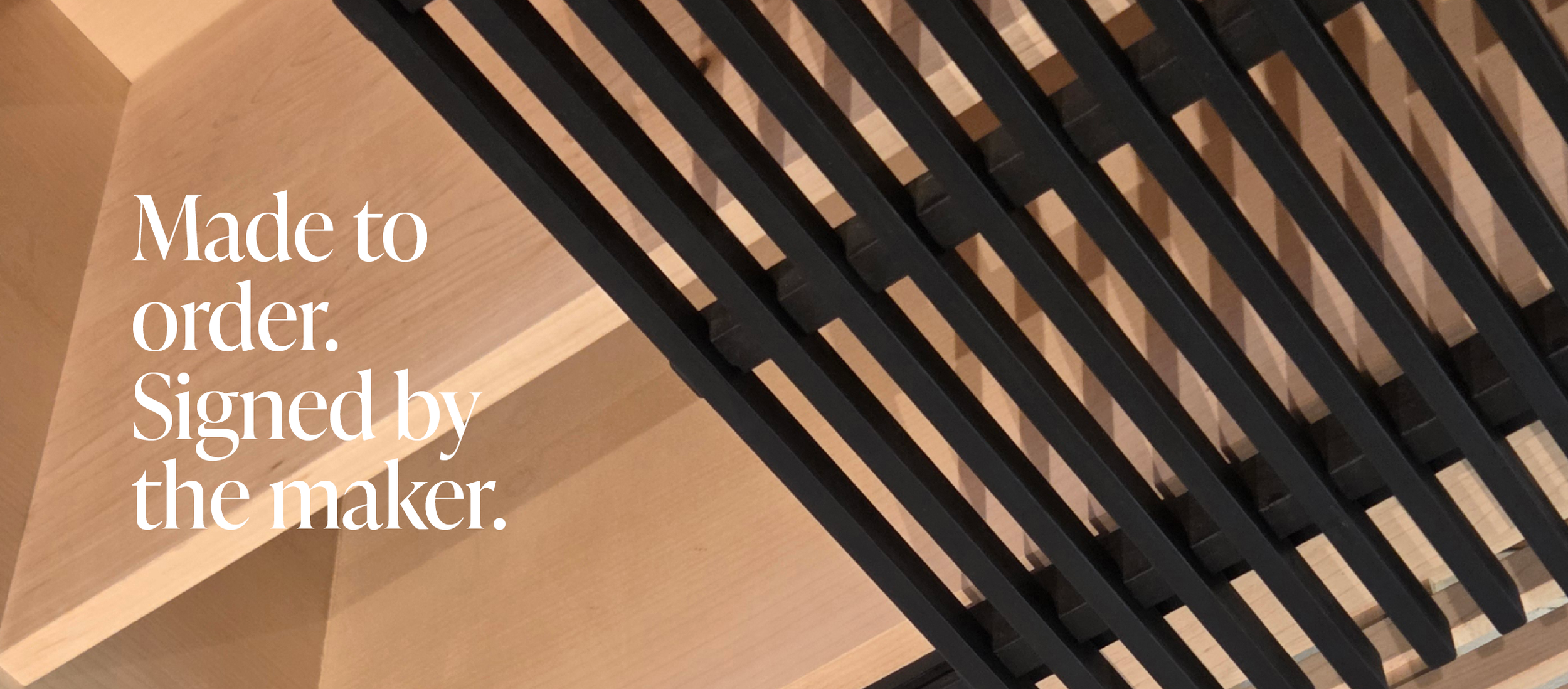 Close-up of a wooden piece with a black slatted surface on top. White text overlay reads "Made to order. Signed by the maker."