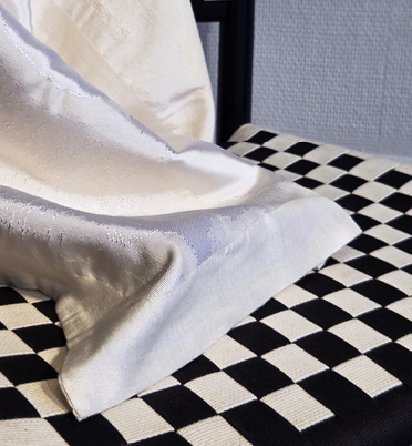 A close-up of a white satin pillow on a black and white checkered fabric surface.
