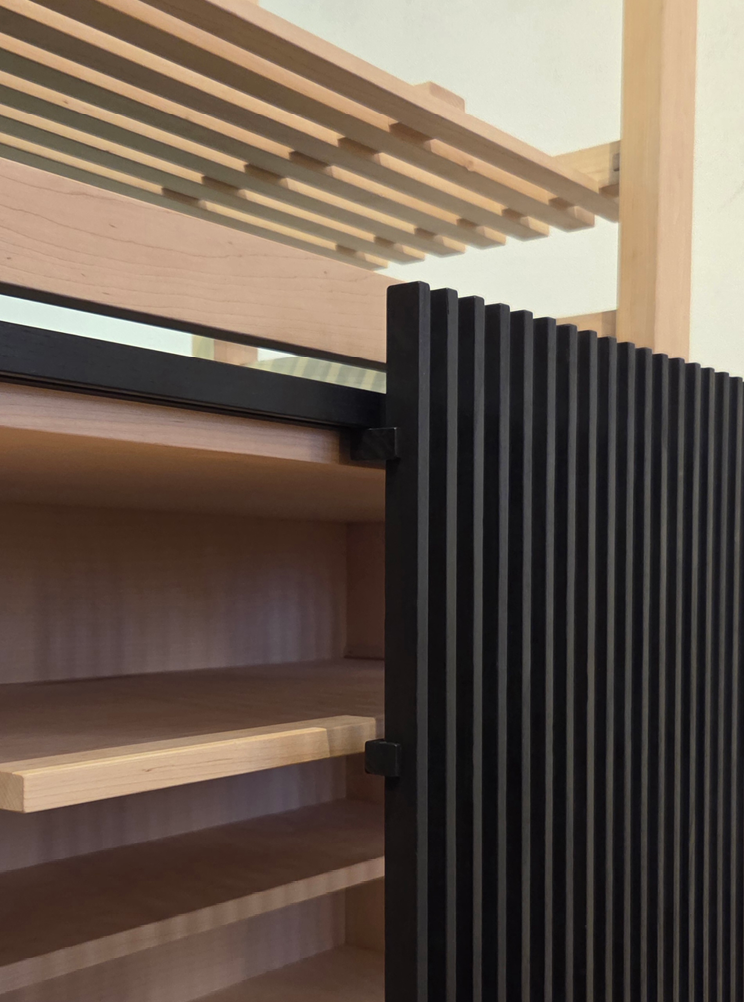 Close-up of a wooden cabinet with black slatted sliding doors and wire shelving on top.