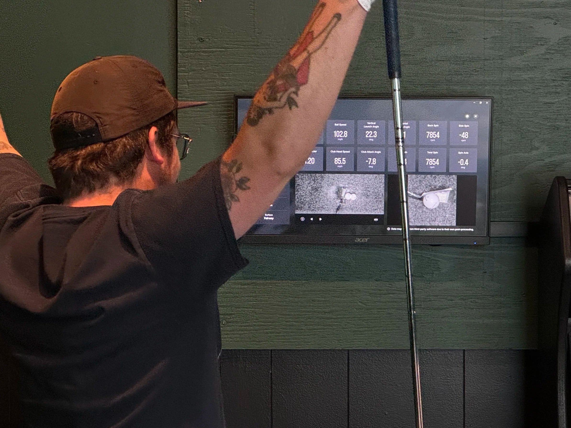 A golfer reviews launch monitor data, slow-motion replay, and clubface impact location on a dedicated swing data display after a shot.