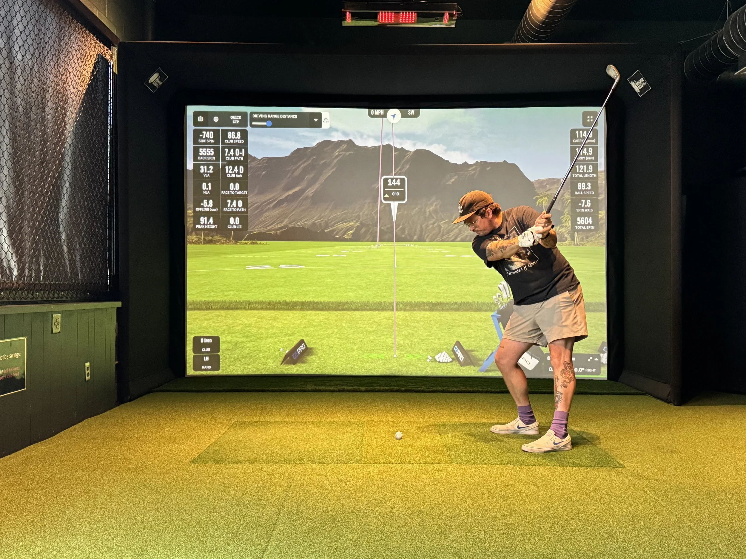 A golfer begins a golf swing inside the Swingers Golf Club simulator while real-time ball flight and launch monitor data are displayed on the impact screen.
