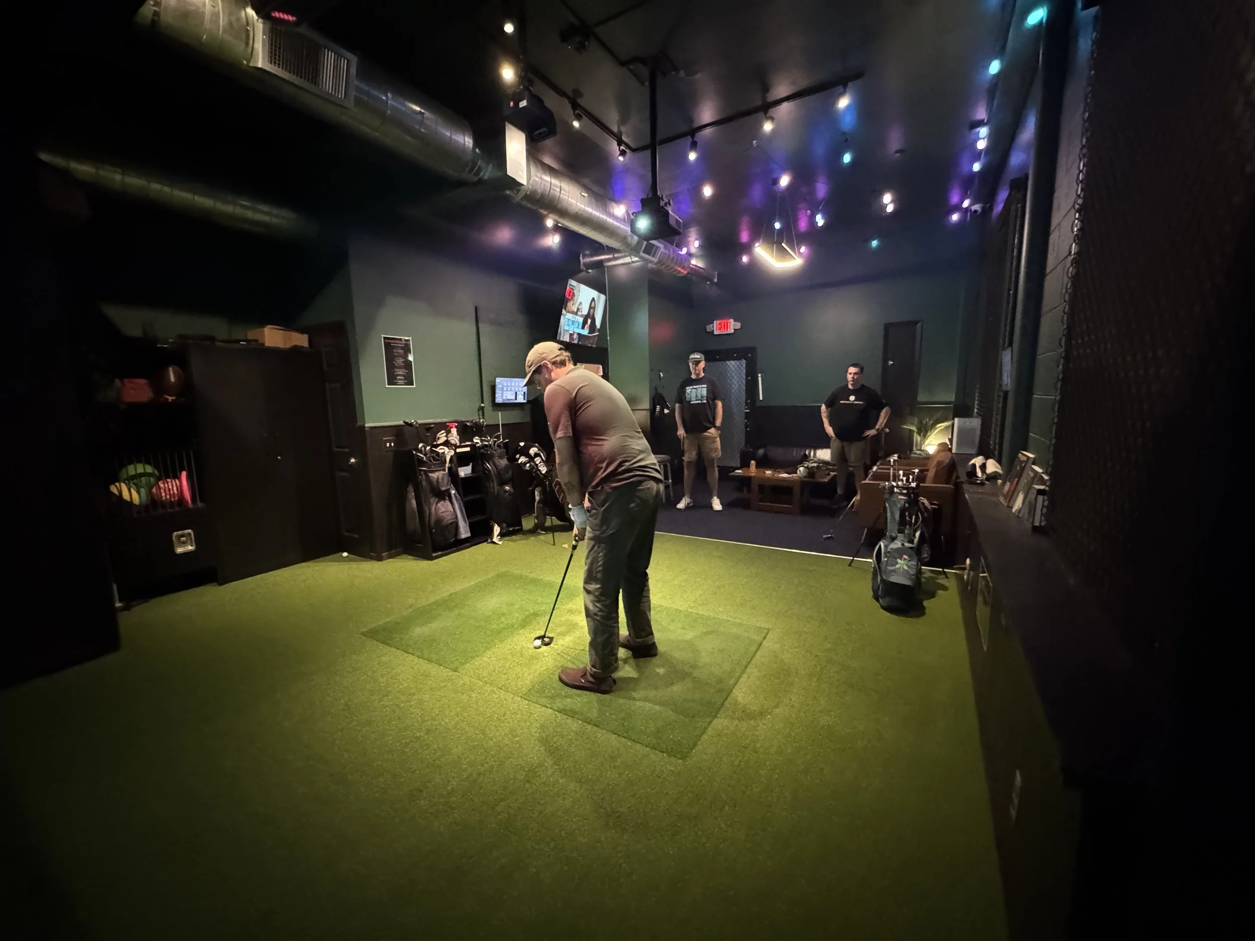 Friends hang out around the simulator and seating area during a private golf session at Swingers Golf Club.